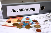 Kleinbetragsrechnung Ein Ordner, auf dem "Buchführung" steht, daneben Kleingeld. Symbolbild zum Thema Kleinbetragsrechnung.