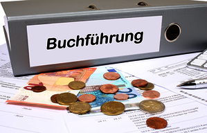 Kleinbetragsrechnung Ein Ordner, auf dem "Buchführung" steht, daneben Kleingeld. Symbolbild zum Thema Kleinbetragsrechnung.