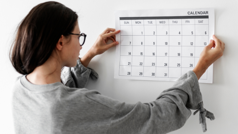 Geschäftsjahr Frau hängt einen Wandkalender auf – symbolisiert die zeitliche Struktur und Planung eines Geschäftsjahrs im Unternehmen.